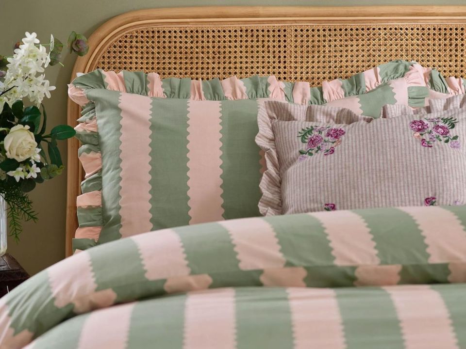 Green and pink striped bedding with ruffled pillows and a woven headboard.