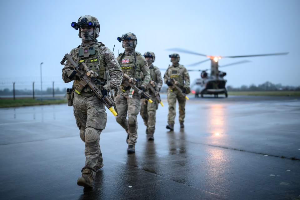 Members of the UK Special Operations Forces walking on an airfield with a Chinook helicopter in the background.