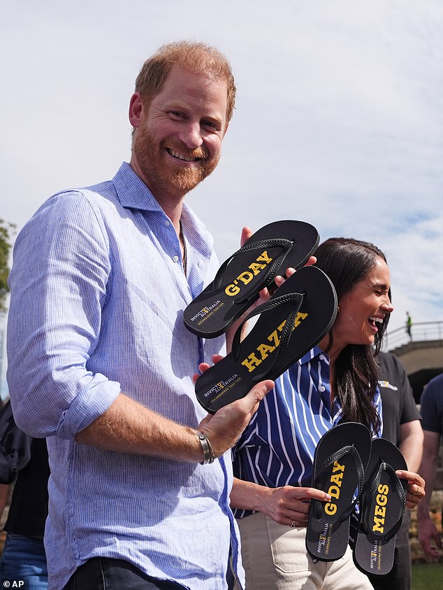 Prince Harry and Meghan, the Duke and Duchess of Sussex, hold flip-flops with the inscriptions 'G' day Hazza' and 'G' day Megs' presented by veteran Joel Vanderzwan as they take part in a sailing event with members of Invictus Australia in Sydney Harbour