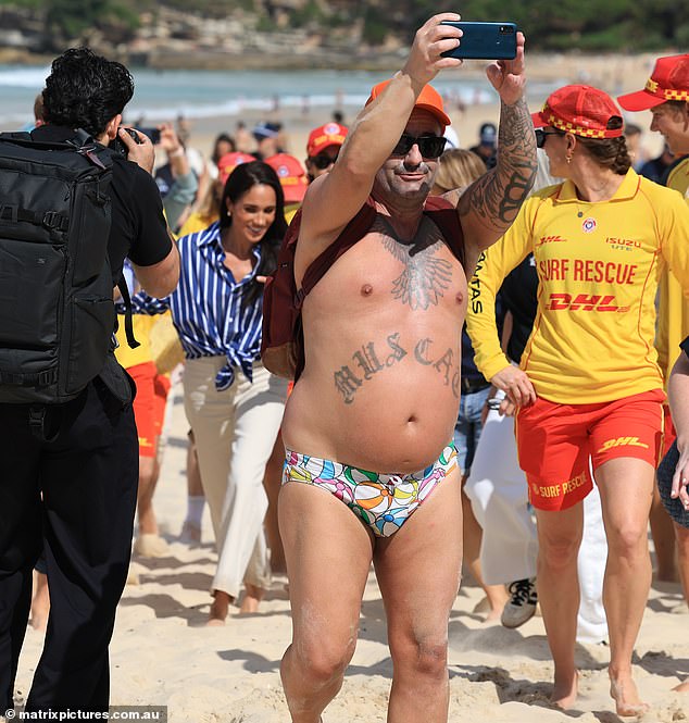 A man clad just in beachball budgie smugglers was taking selfies in front of Prince Harry and Meghan Markle on Bondi Beach