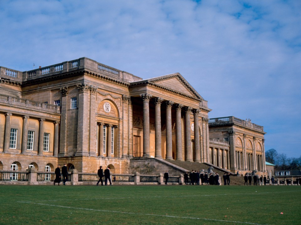 The exterior of Stowe School, a grand Neoclassical building with numerous columns, staircases, and students on the lawn in front.