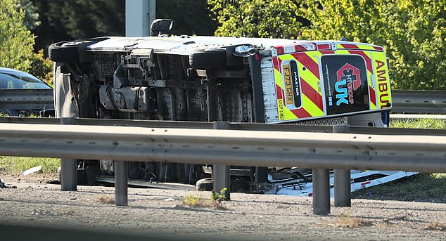 Shocking images (pictured) show an ambulance overturned on its side alongside a flat-bed truck and a large black four-by-four car in the middle of the carriageway