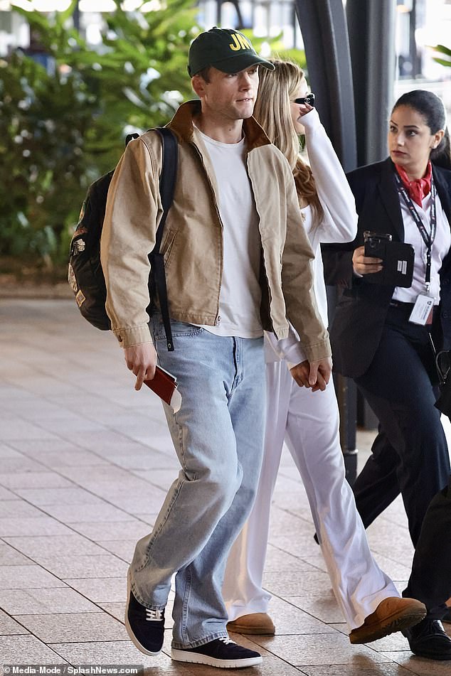 Walking beside her Taron opted for a green baseball cap, with a bomber jacket and jeans for the trip