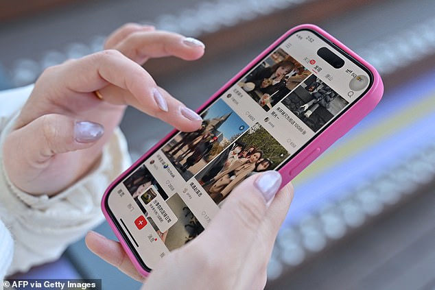 A woman holds her smartphone displaying the Chinese social networking app RedNote