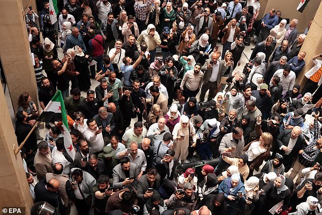 The disgraced official, whose head is shaved and hands are handcuffed, perched on the corner of a wooden bench as hordes of people filmed and took pictures of him through the metal bars