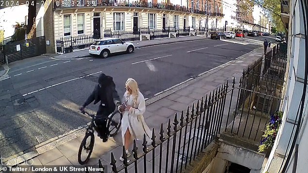 A thief steals a phone from a woman walking down a road in London's exclusive Mayfair area