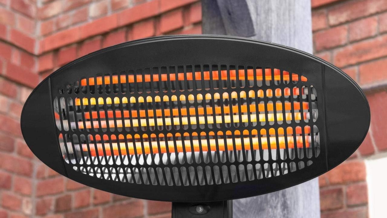 A black oval-shaped patio heater with glowing orange and yellow bars inside, set against a brick wall.