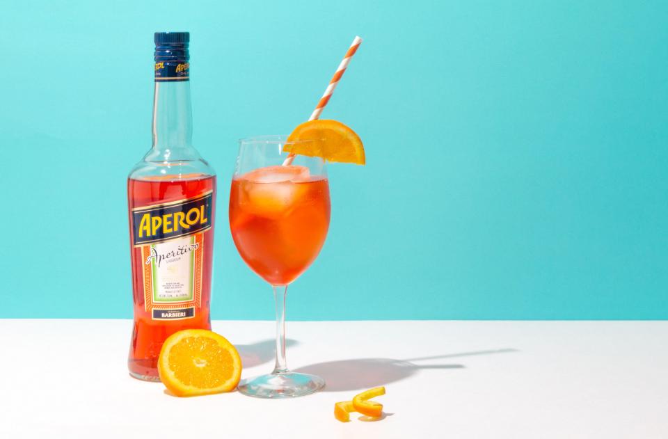 A bottle of Aperol and an Aperol Spritz cocktail in a stemmed glass with an orange slice and straw.