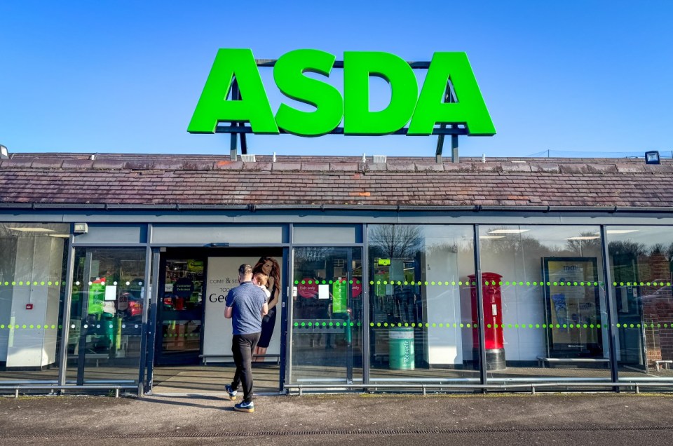 A man carrying a baby walks towards the entrance of an ASDA supermarket.