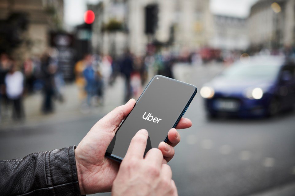 A person holding a smartphone with the Uber app open, with a blurry street and cars in the background.