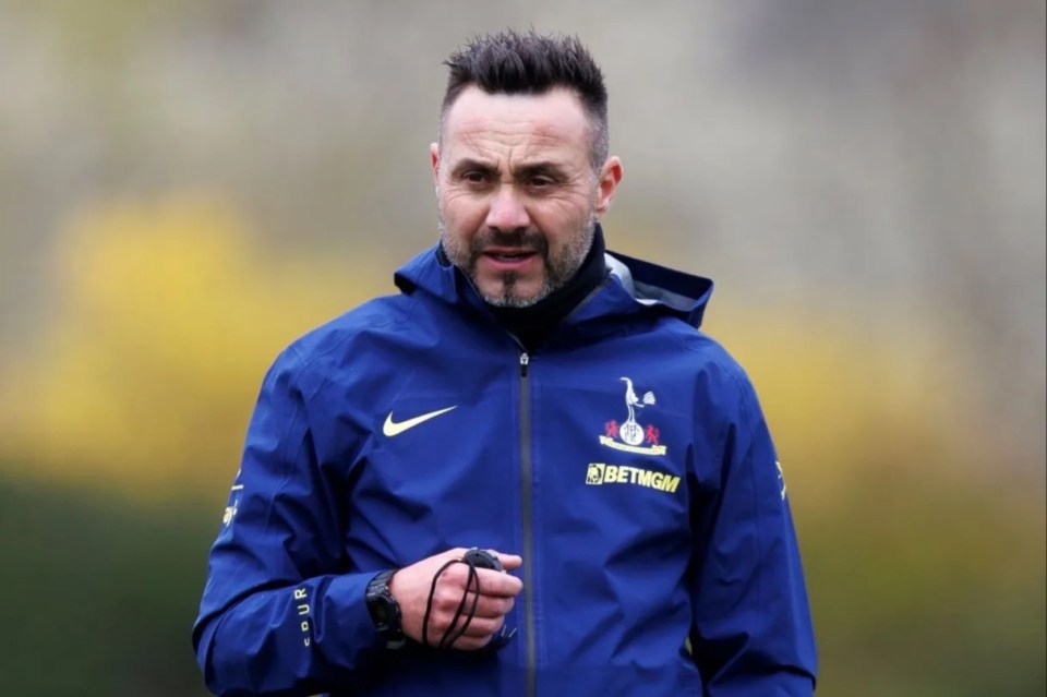 A man in a blue Tottenham Hotspur training jacket holds a stopwatch.