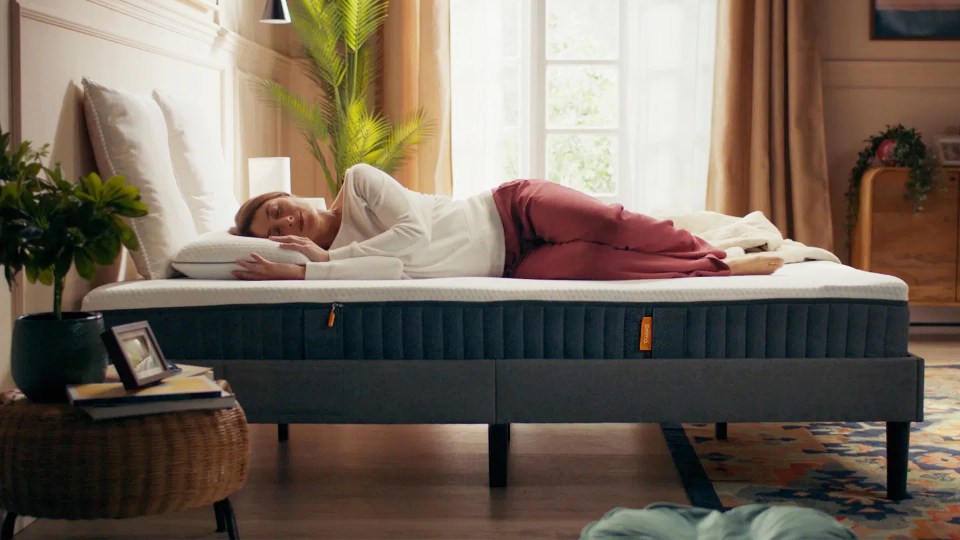 A woman sleeping on her side on a white mattress on a bed frame.
