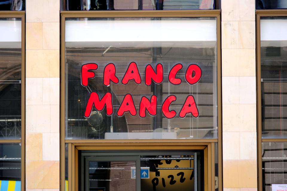 Franco Manca shop sign with "FRANCO MANCA" in red block letters visible through a shop window.