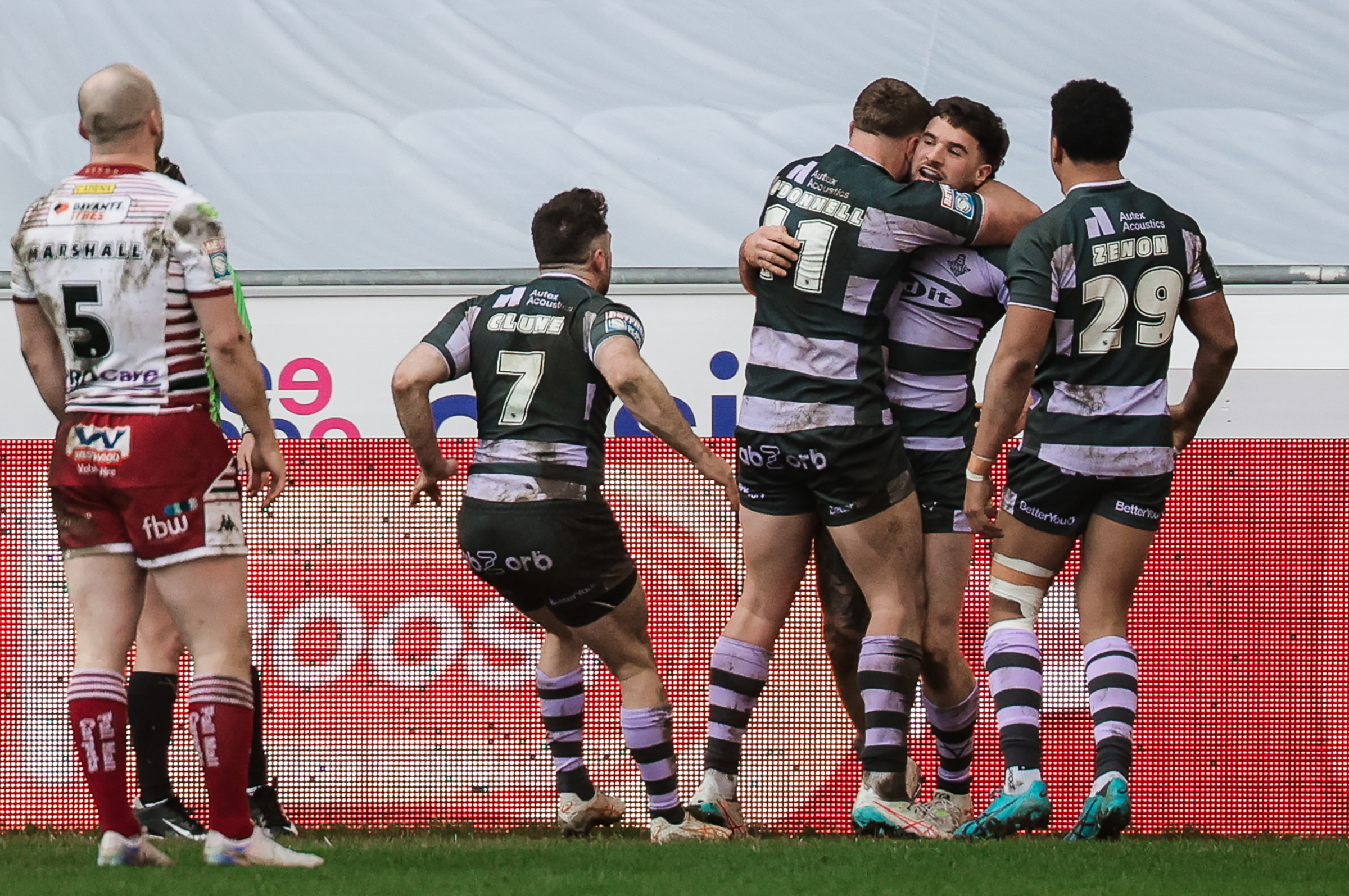 Rugby players in maroon and white and dark green and light purple uniforms on a field.