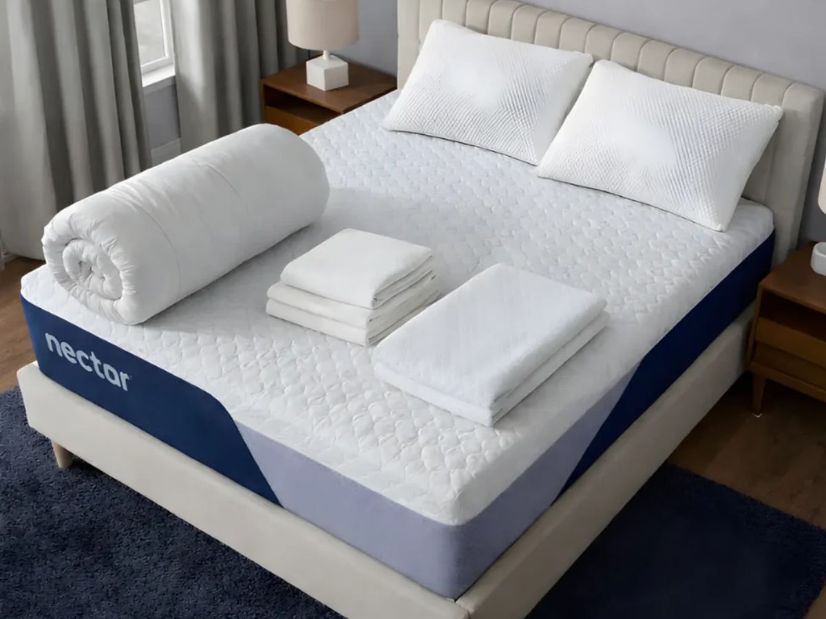 A Nectar mattress with two pillows, a rolled-up comforter, and two sets of folded sheets.