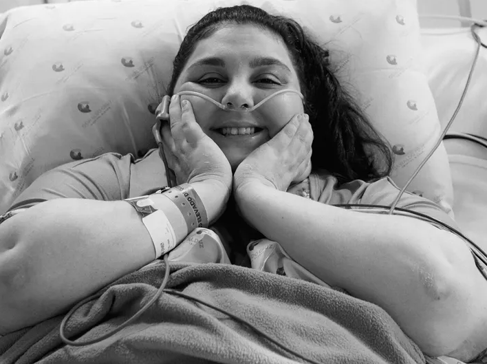 A person with a nasal cannula and hospital bracelet smiles at the camera.