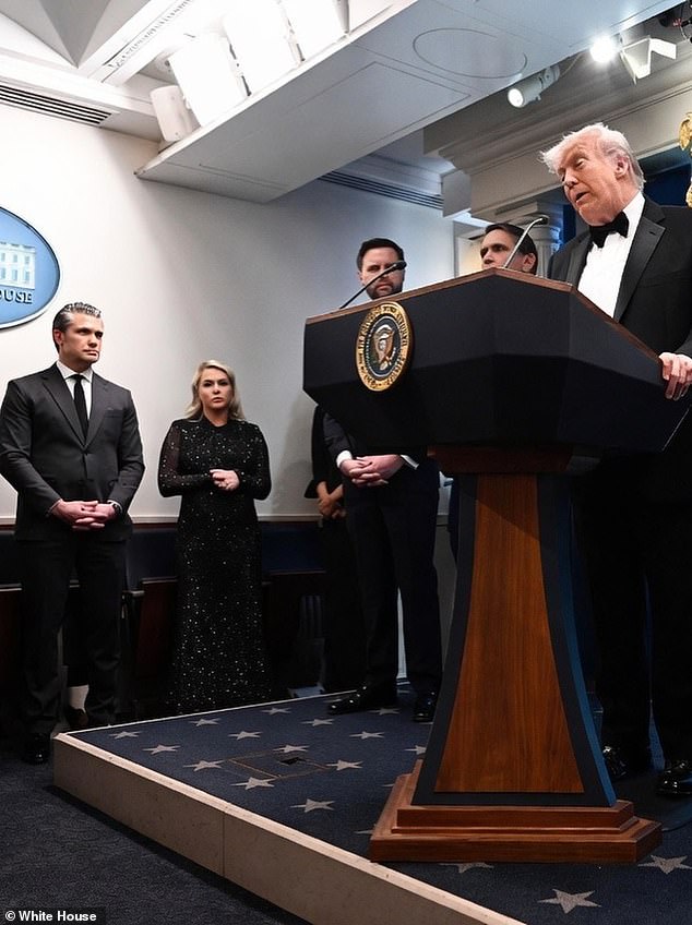 Karoline Leavitt off to the side in the White House press briefing room as Trump delivers remarks