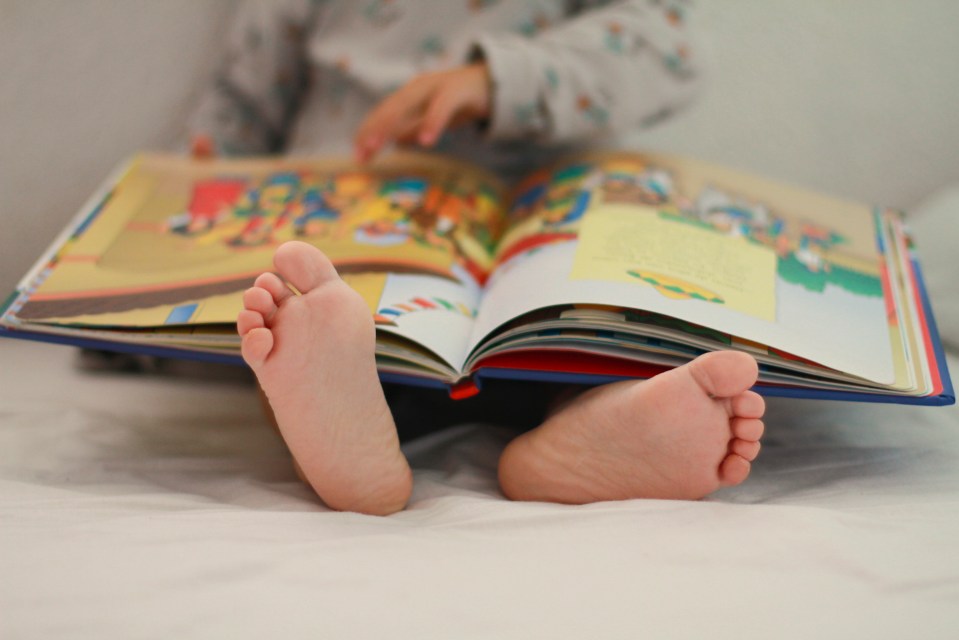 Child's feet on a bed with a colorful picture book open in the background.