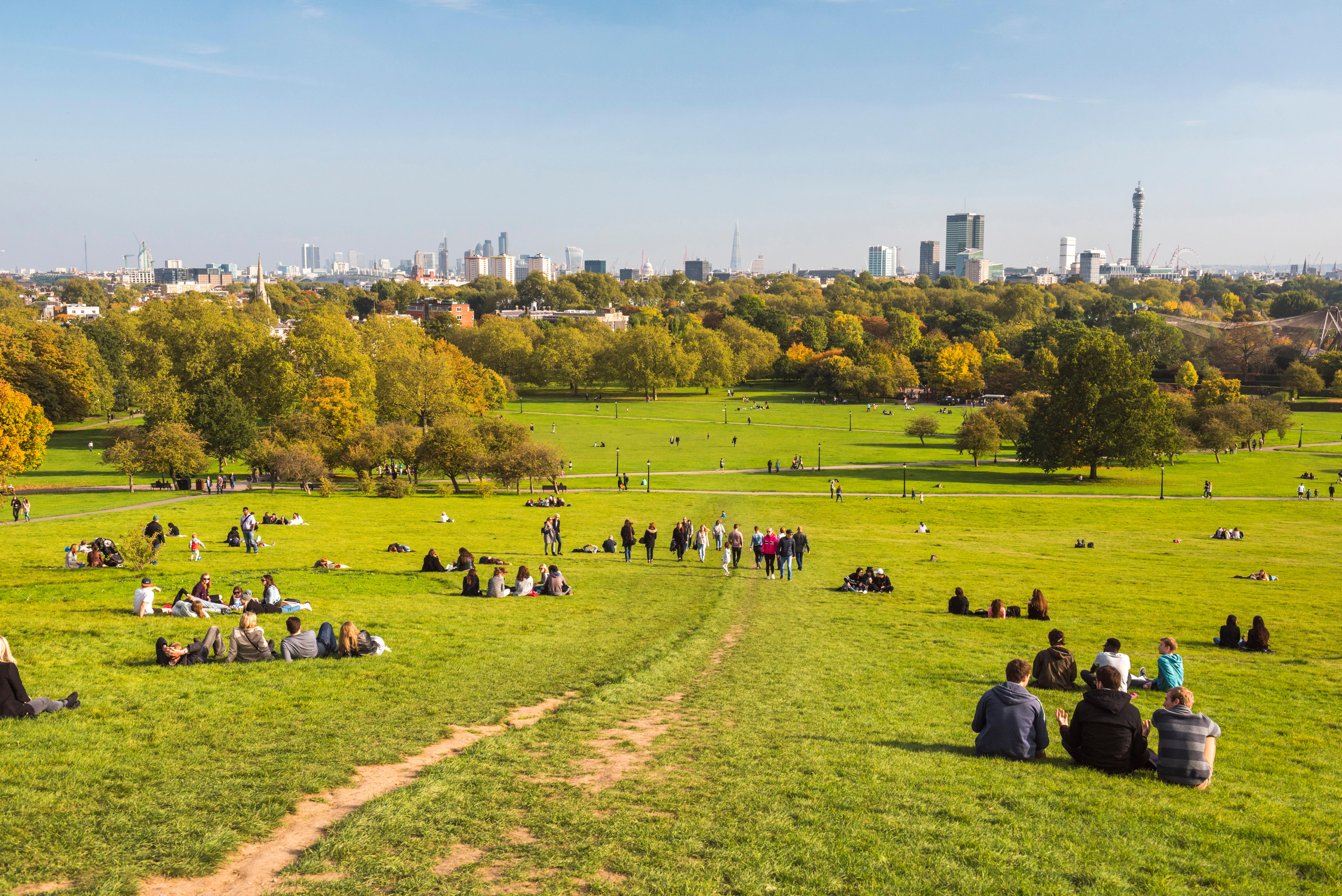 People relaxing on a grassy hill with the London skyline in the distance during autumn.