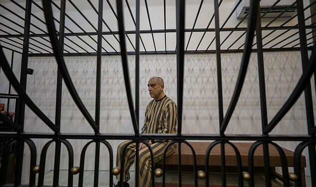 Atef Najib, wearing a striped prison uniform, sat seemingly emotionless on Sunday in a cage in a courtroom in Central Palace of Justice, in Syria's capital, Damascus
