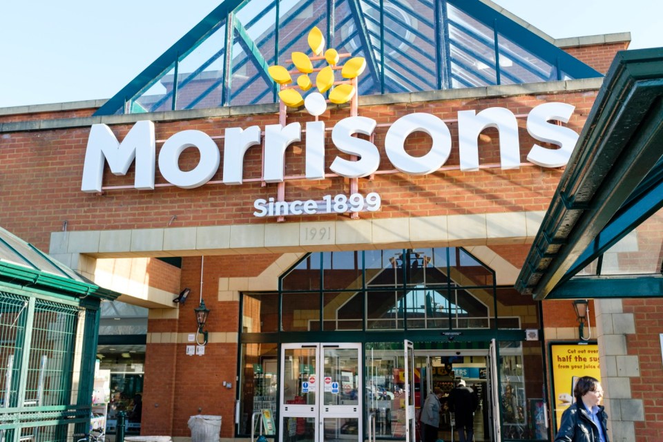 The front exterior of a Morrisons supermarket with its large white sign and yellow logo on a brick wall.
