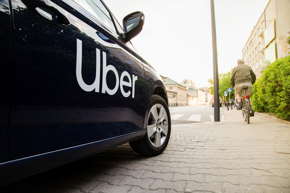 Side view of a dark Uber car parked on a street with a cyclist in the background.