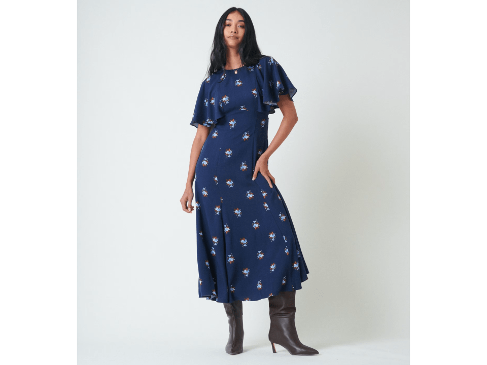 A woman wearing a dark blue midi tea dress with small floral patterns and brown boots.