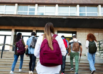 Students walk up the steps of a schoolhouse.