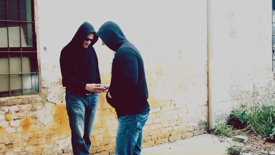 Two men in hoodies and jeans exchange money for drugs.