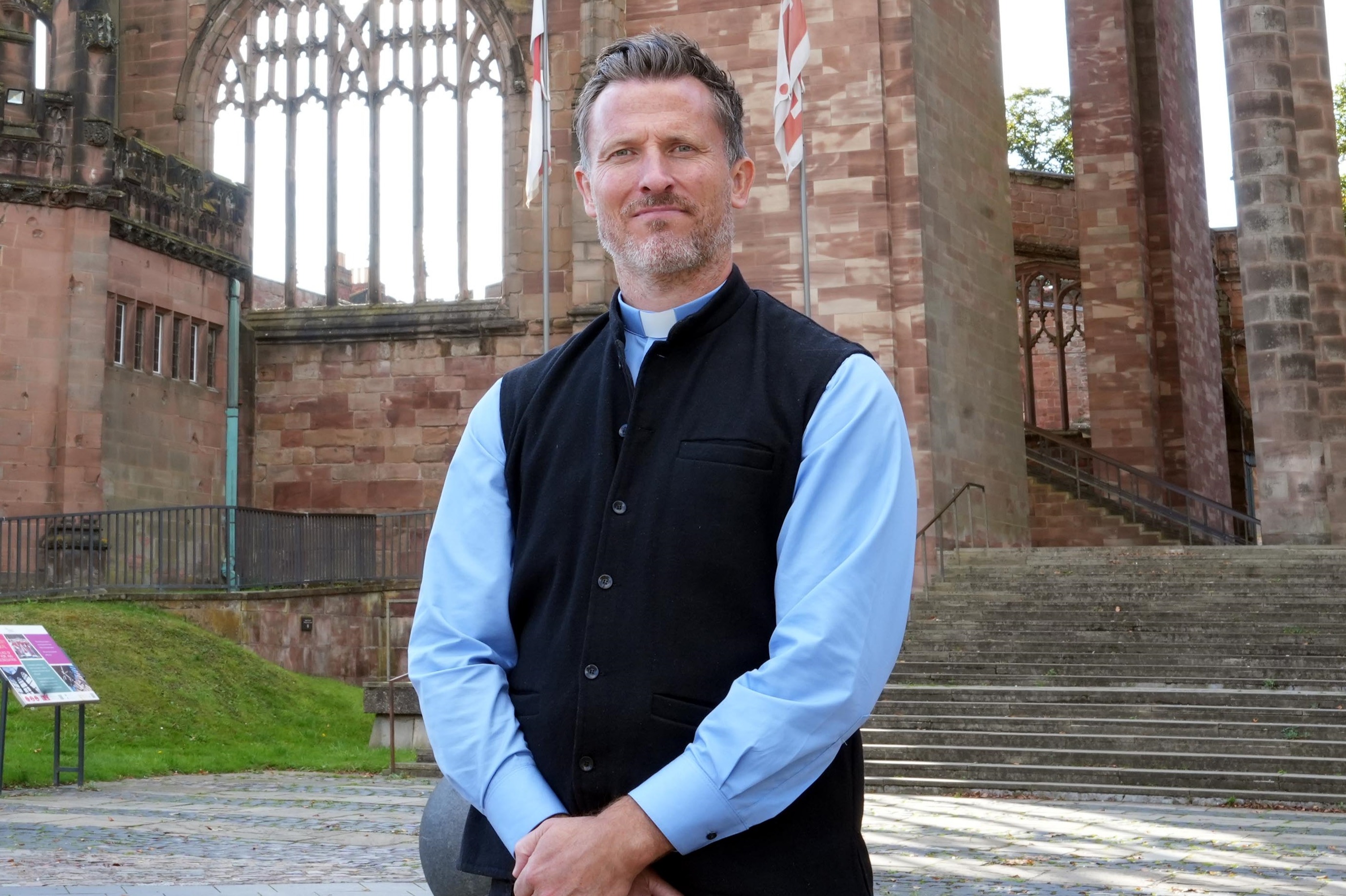 Rev. Pat Allerton standing outside a historic church with Gothic architecture.