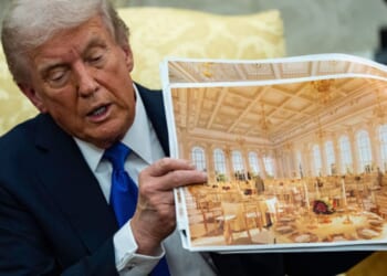 President Trump sits in the Oval Office on October 22, 2025 as he displays photos of the White House ballroom plans.