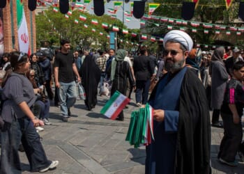 A man offers Iranian flags as people walk by near the Tehran Grand Bazaar Thursday in Tehran, Iran.