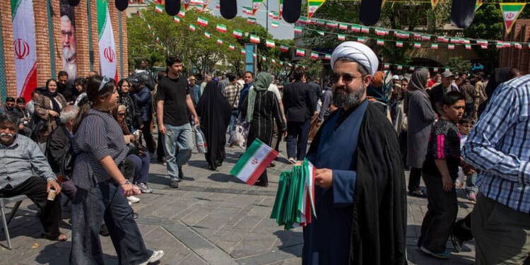 A man offers Iranian flags as people walk by near the Tehran Grand Bazaar Thursday in Tehran, Iran.
