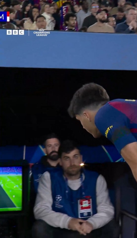 A footballer leans over to talk to a man in a blue vest with a UEFA Champions League logo.