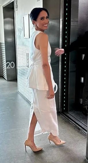 Meghan Markle smiles as she wears a white co-ord outfit as she enters a lift
