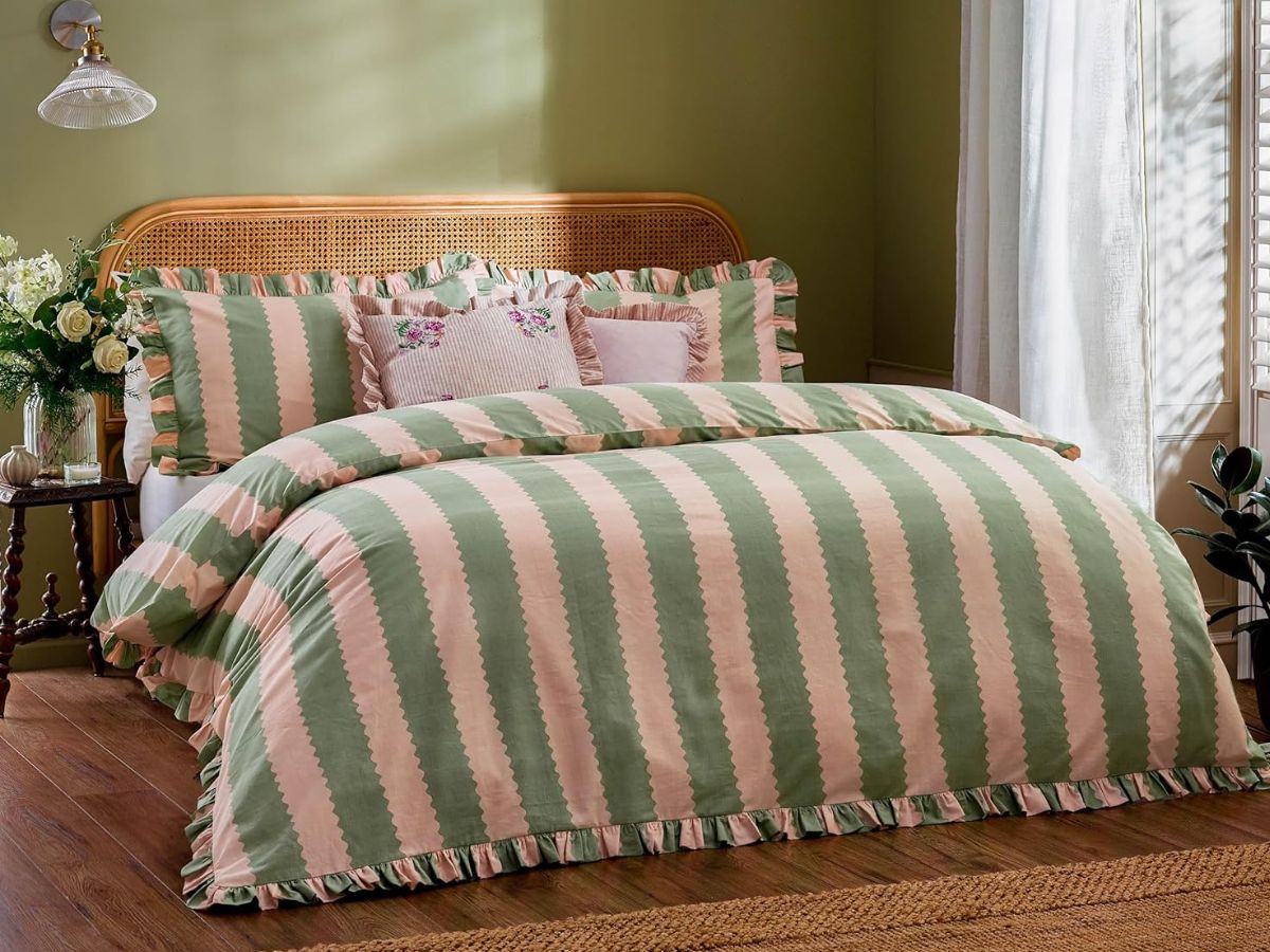 Green and pink striped bedding with ruffled edges on a wooden bed.