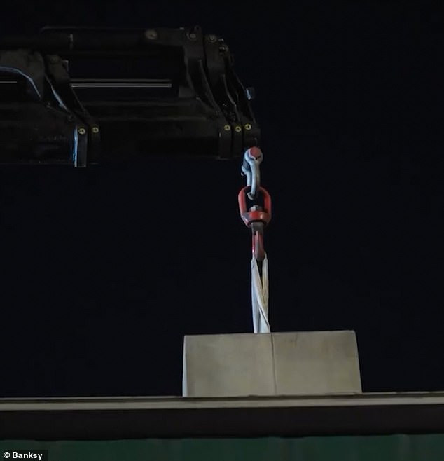 A large metal hook and a hydraulic crane are used to erect the plinth and position the statue