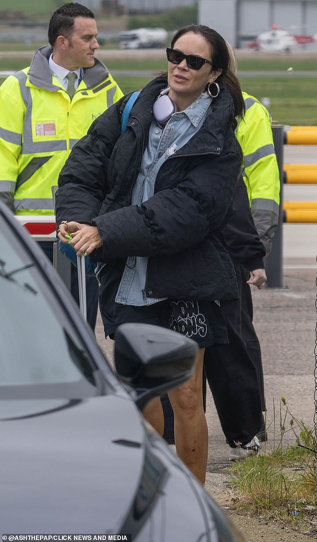 Comedian Joanne McNally was also seen on the same flight, dressed in cycling shorts and also hiding behind some dark shades as she wheeled her luggage to the car