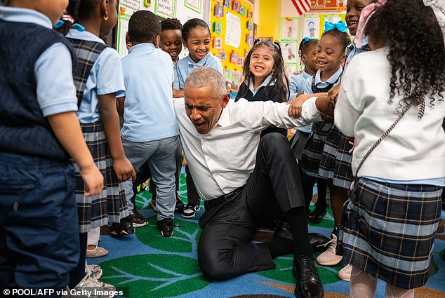 Obama pretends to struggle to stand as children lift him up during a visit to Learning Through Play Pre-K in New York on April 18