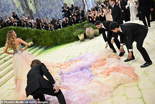 As one of the men helping her starts to lift up the skirt, she suddenly turns over her shoulder and puts her hand out toward the skirt.