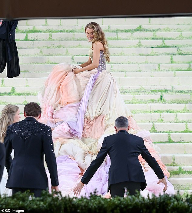 A single helper remains at her side and fidgets with her dress and tries to give her an arm to hold on to for balance, but Lively turns back to him and seems to wave him away, at which point he departs as well to leave her to pose for photographers by herself