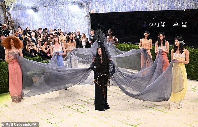 The ladies were helping carry the singer's long veil. Her look was inspired by a 1945 painting called The Temptation of St. Anthony. Fragment II, a Surrealist masterpiece by Leonora Carrington