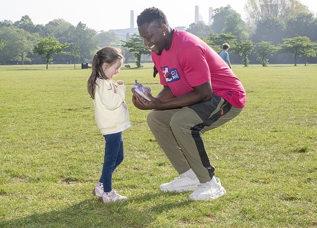The England rugby captain is pictured handing over a tiny pair of trainers to a young fan with Battersea Power Station visible in the distance