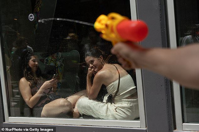 People at a restaurant watch as a protestor uses a water gun toward the window during an anti-tourism demonstration in Barcelona