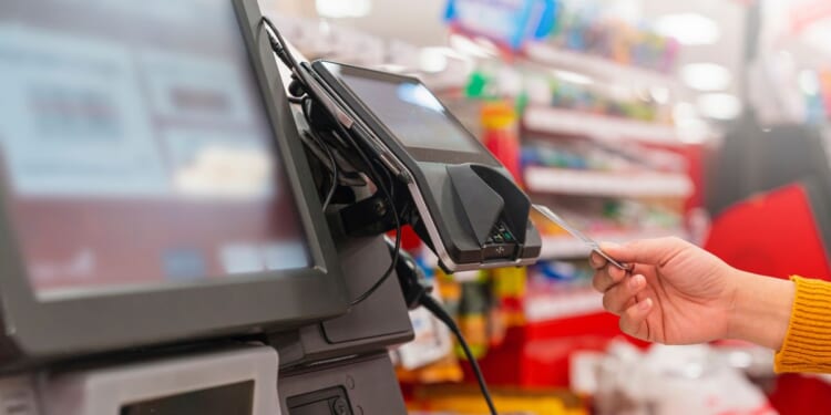 A person uses a card to pay at a grocery store self-service kiosk.