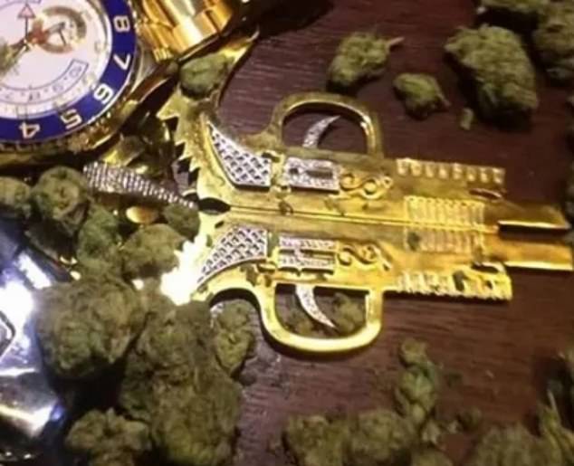 In this photo, a fearsome looking weapon lies on a table next to a luxury watch and a large amount of cannabis