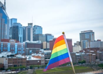 A rainbow flag flies in the foreground with the city of Nashville in the background.
