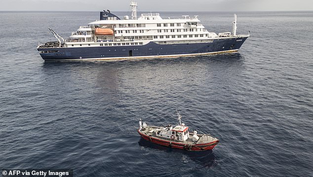 An aerial view of an ambulance boat carrying crew members wearing hazmat suits as they approach the pilot door on the starboard side of the cruise ship MV Hondius