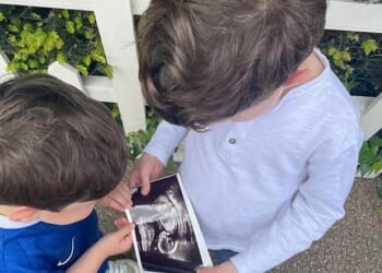 In a photograph shared by Princess Eugenie today, Ernest, wearing a Chelsea football kit, and August, wearing a long-sleeved grey t-shirt, can be seen holding a picture of a baby scan