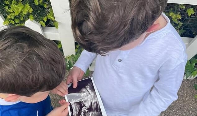 In a photograph shared by Princess Eugenie today, Ernest, wearing a Chelsea football kit, and August, wearing a long-sleeved grey t-shirt, can be seen holding a picture of a baby scan